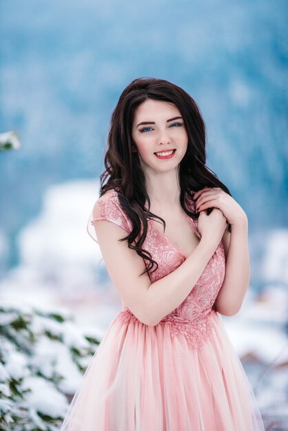 Chica con cabello castaño, ojos azules y un vestido rosa en el fondo de las montañas de invierno