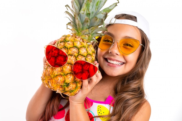 Chica con cabello largo crucificado en gafas de sol y traje de baño se juega con piña en gafas de sol