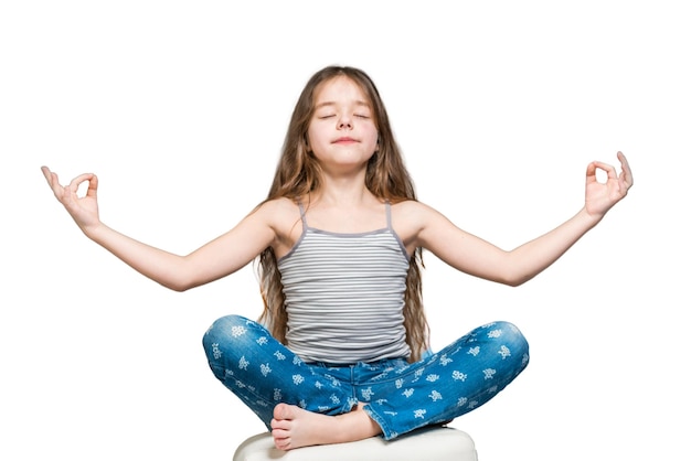 Chica con cabello largo y jeans meditando en una pose de loto sobre un fondo blanco Aislado