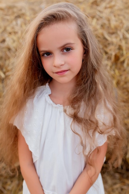 una chica con cabello largo y ojos grandes con un vestido blanco en un campo de trigo