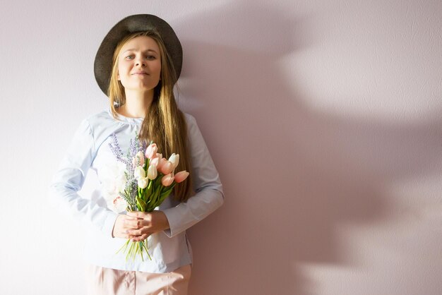 chica con cabello largo rubio disuelto un sombrero de fieltro en la cabeza guarda flores