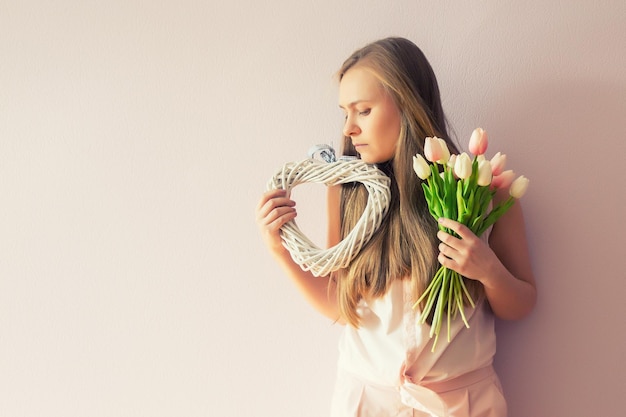 chica con cabello largo rubio disuelto un sombrero de fieltro en la cabeza mantiene flores de primavera en sus manos