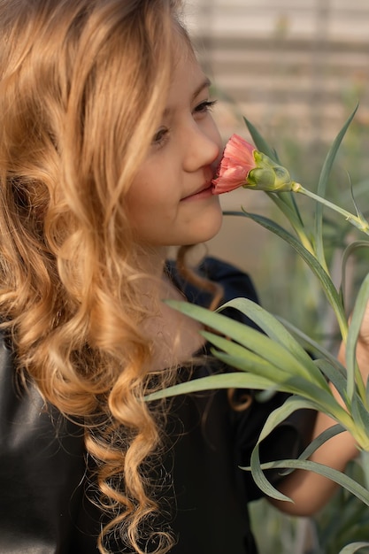 Una chica con cabello largo y rubio oliendo una flor.