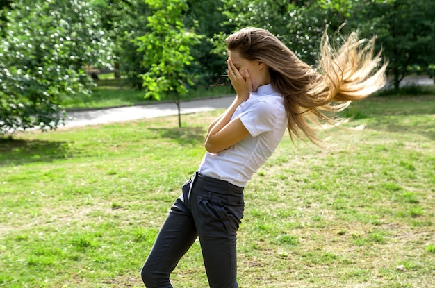 Chica con cabello largo y rubio se ríe y cubre su rostro con sus manos Park risa de alegría al aire libre