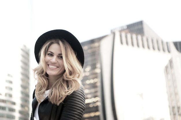 Chica con cabello largo con sombrero negro, sonrisa de chaqueta de cuero en parís, francia en entorno urbano. Estilo de vida, vacaciones, viajes. Moda, estilo, concepto de belleza.