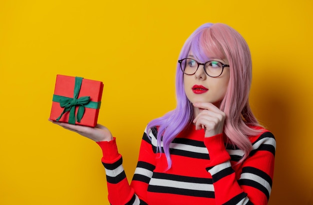 Chica con cabello morado en suéter de rayas rojas con caja de regalo sobre fondo amarillo