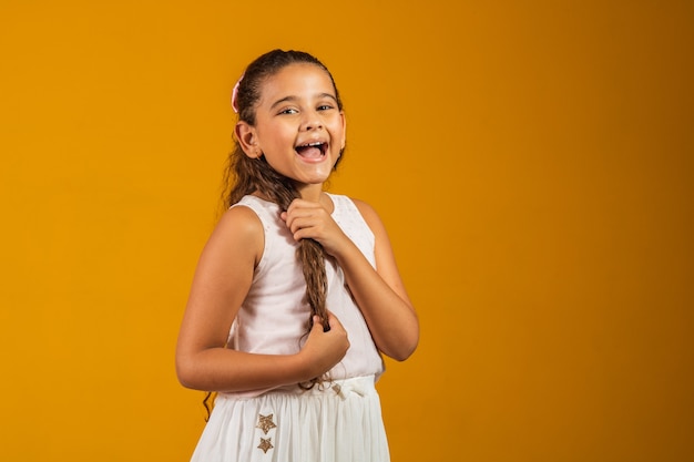 Chica con cabello ondulado largo sano. Belleza, mirada, peinado. Modelo infantil con sonrisa en cara linda sobre fondo amarillo. Niño feliz, concepto de infancia. Juventud, cuidado y salud.