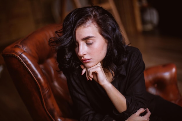 Chica con cabello oscuro rizado y maquillaje natural sentada en una silla de cuero procesamiento de fotos vintage