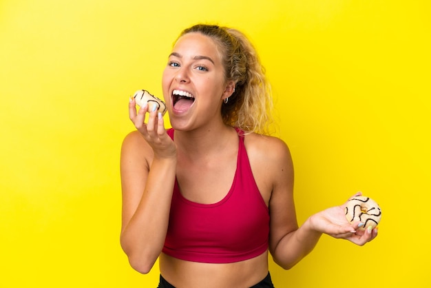 Chica con cabello rizado aislado sobre fondo amarillo comiendo un donut