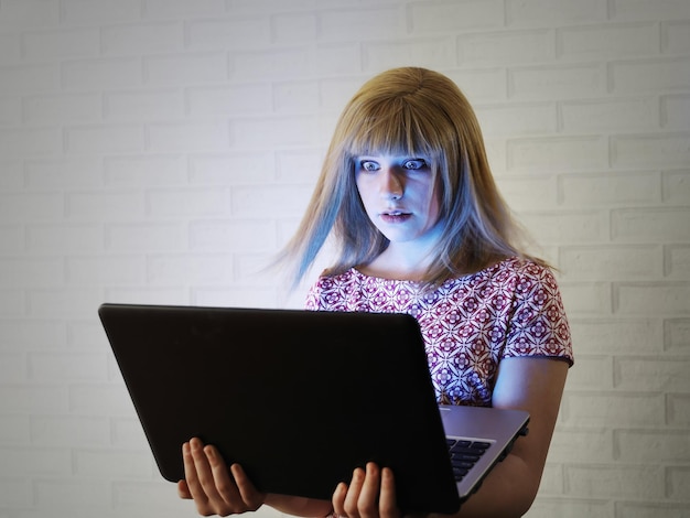 Chica con cabello rubio abre ampliamente los ojos desde la pantalla del portátil con luz azul