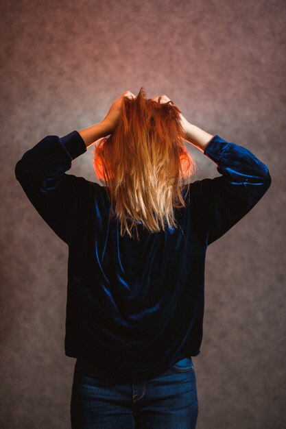 Chica con cabello rubio posando emocionalmente sobre un fondo gris. Su cabello está iluminado en rojo