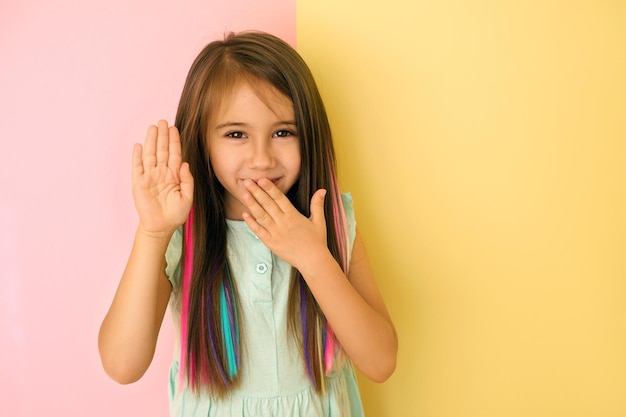 Chica con cabello teñido se ríe tapándose la boca con la mano y muestra un gesto de alto con la palma