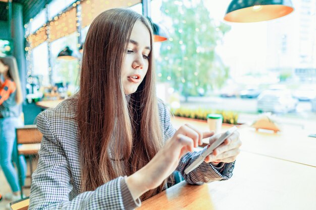 Una chica en un café está tocando la pantalla táctil de su teléfono celular