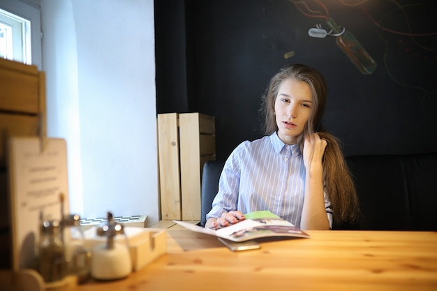 Chica con café. Hermosa joven está sentada en un café y tomando café en un vaso de papel. La niña está desayunando en la cafetería.