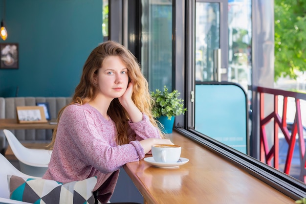 Chica en un café con una taza de café, sonriendo.