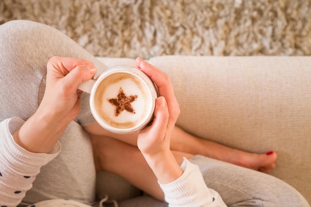 Chica con café con taza de estrella de canela sentada en el sofá en el interior