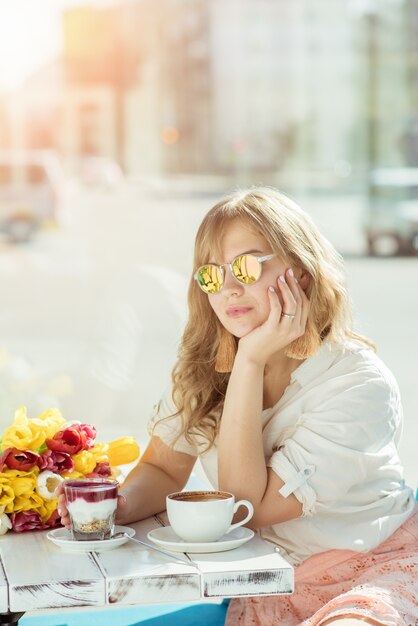 Chica en una cafetería de verano con yogurt y café.