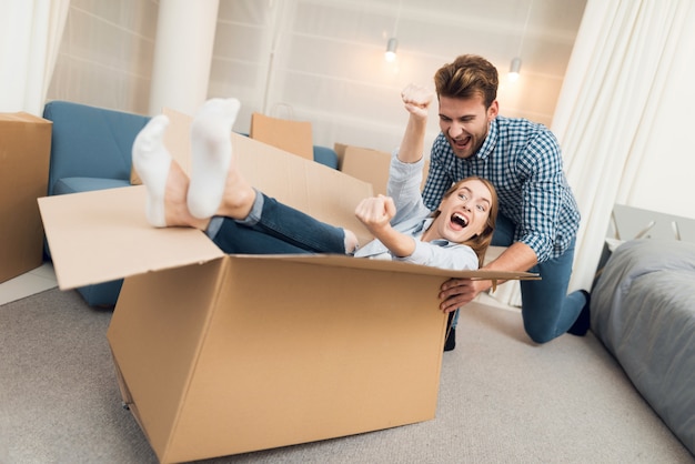 Chica en una caja y un chico la está rodando por el apartamento