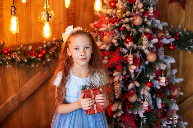 Chica con caja de regalo cerca de árbol de Navidad