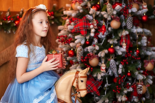 Chica con caja de regalo cerca del árbol de navidad