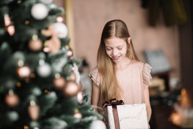 Chica con una caja de regalo de pie cerca del árbol de Navidad