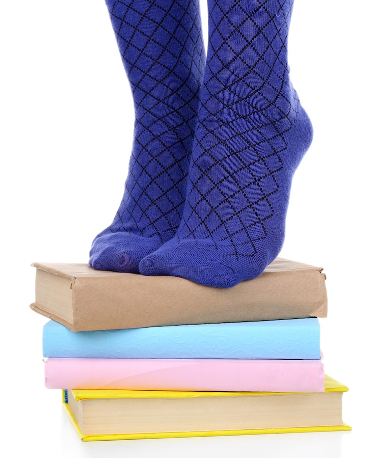 Foto chica en calcetines coloridos de pie sobre un montón de libros aislados en blanco