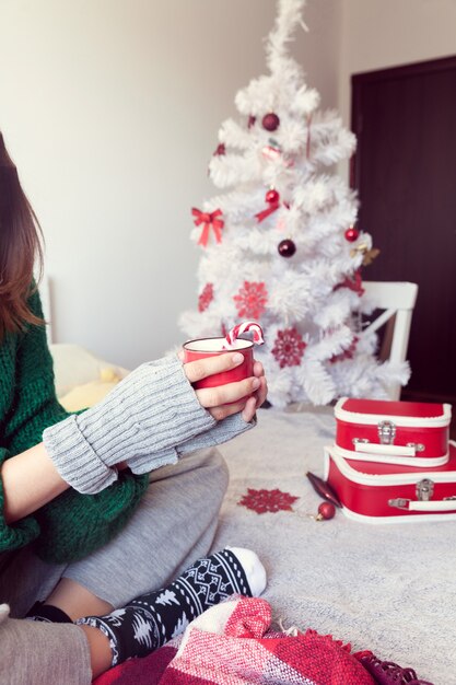 Chica en calcetines de Navidad sosteniendo una taza de café en el fondo del árbol de Navidad