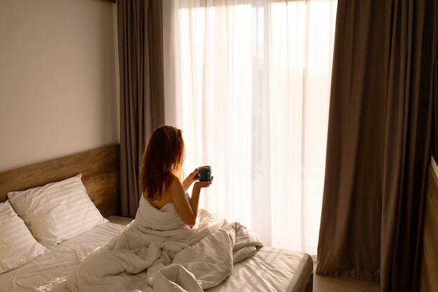 Chica en la cama con café por la mañana con té en la cama despertando a una chica en ropa de cama blanca con café