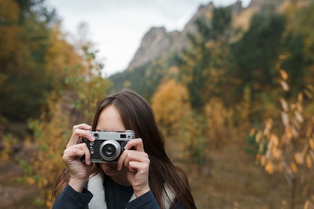 Chica con cámara retro en las montañas de otoño