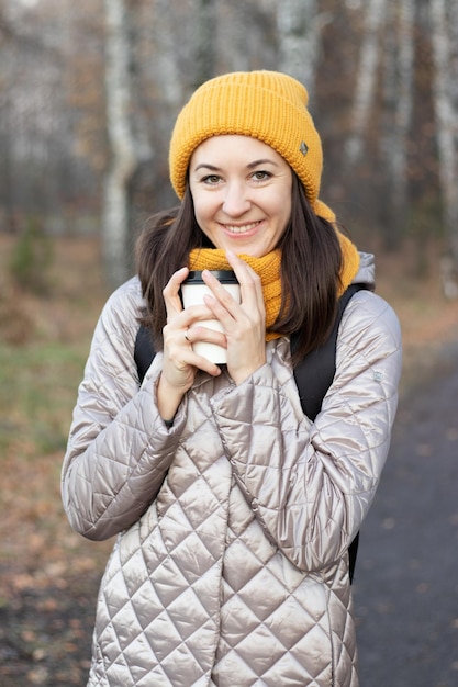 Chica camina en el parque de otoño con una taza de café