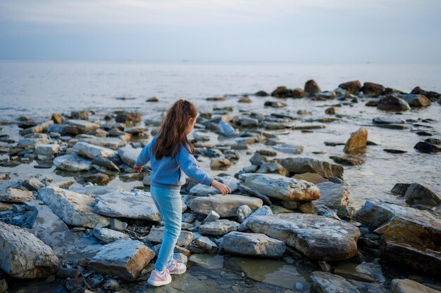 Foto una chica camina por una playa rocosa con el mar de fondo.