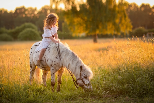 Chica caminando al atardecer en un campo con un caballo