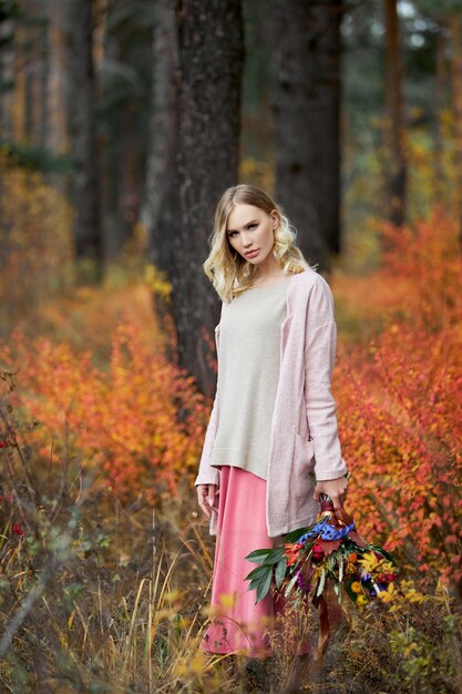 Chica caminando en el bosque de otoño. Un gran ramo de flores en manos de una mujer. Chica se encuentra en la hierba roja amarilla, naturaleza otoñal