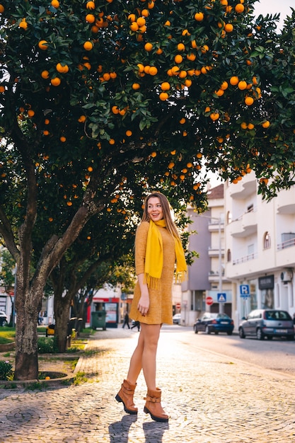 Chica caminando por las calles vestida. árboles con naranjas. ciudad.