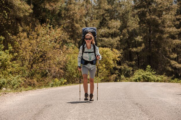 Chica caminando en el camino con mochila de senderismo y bastones de senderismo