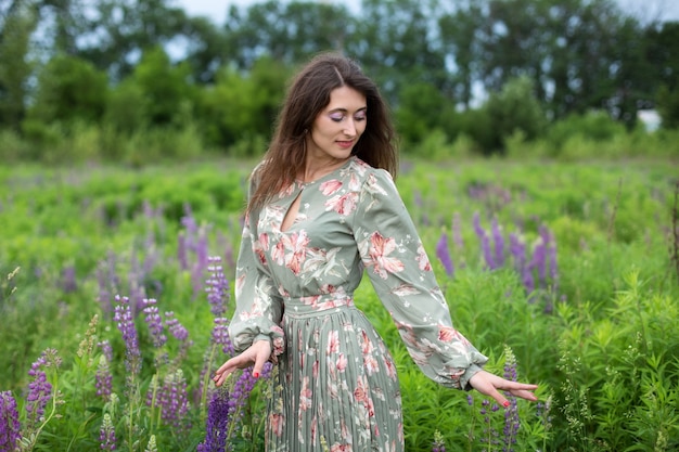 Chica caminando en el campo de verano con flores silvestres mujer vestida en campo floreciente de altramuces