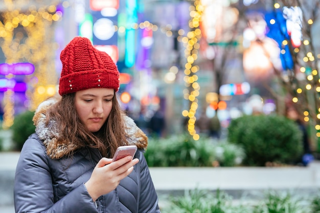 Chica caminando y enviando mensajes de texto en su teléfono inteligente