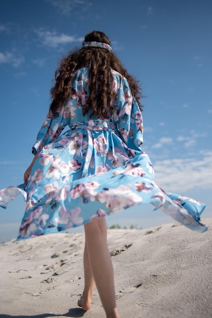 Una chica caminando por la playa con un vestido azul.