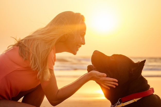 Chica caminando con su gran perro Cane Corso negro en la playa del mar del océano índico en Goa al atardecer