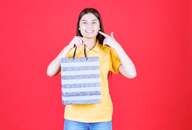 Chica en camisa amarilla sosteniendo una bolsa azul con patrones en ella