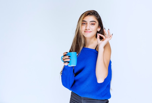 Chica de camisa azul tomando una taza de café y disfrutando del sabor.