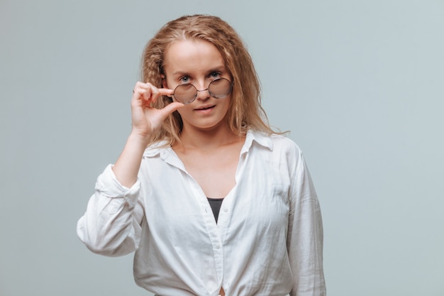 Chica con camisa blanca y gafas redondas sobre fondo gris