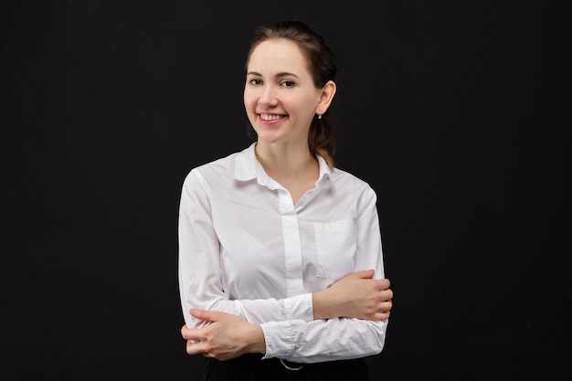 Chica con una camisa blanca mirando a la cámara y sonriendo sobre un fondo negro.