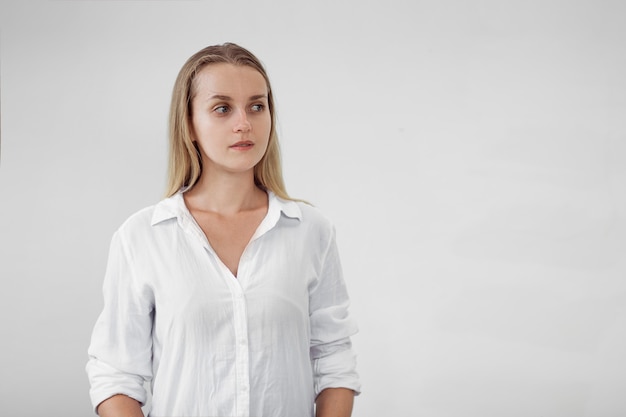 Chica con camisa blanca en la pared de luz mirando a la derecha, espacio de copia