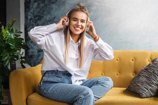 Chica con camisa blanca se sienta en el sofá y disfruta de la transmisión de audio.