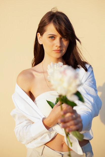 Chica con una camisa blanca tiene una flor blanca en la mano sobre un fondo beige