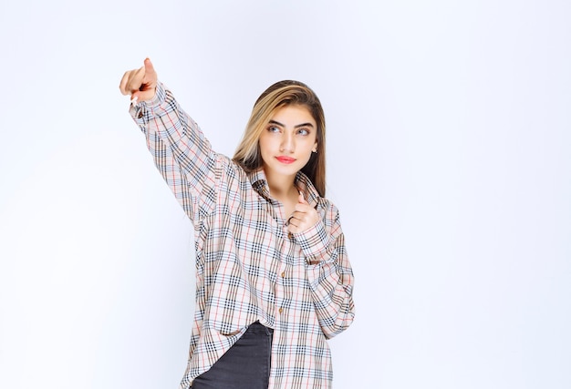 Chica en camisa a cuadros apuntando a alguien alrededor