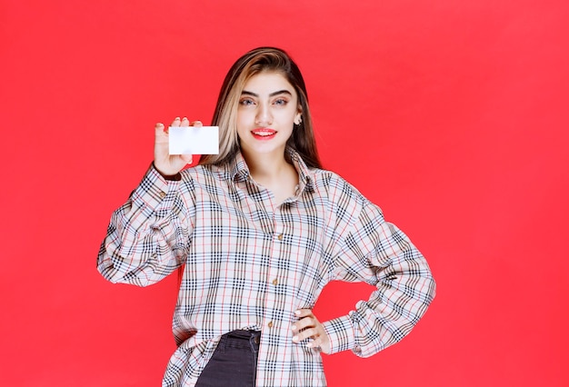 Chica en camisa de cuadros presentando su tarjeta de visita