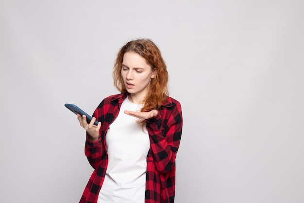 Chica con una camisa a cuadros sobre un fondo claro con un teléfono inteligente