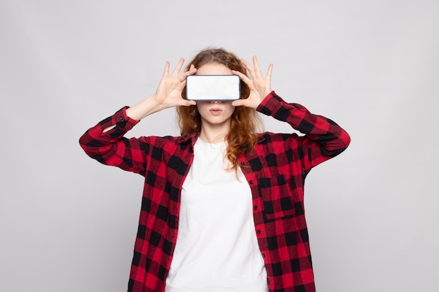 Chica con una camisa a cuadros sobre un fondo claro con un teléfono inteligente